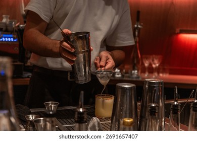 Bartender is skillfully preparing a cocktail using a shaker and strainer in a stylish bar, showcasing mixology expertise and vibrant atmosphere.