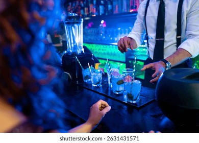 Bartender skillfully preparing vibrant blue cocktails garnished with fresh mint and ice in a lively nightclub atmosphere