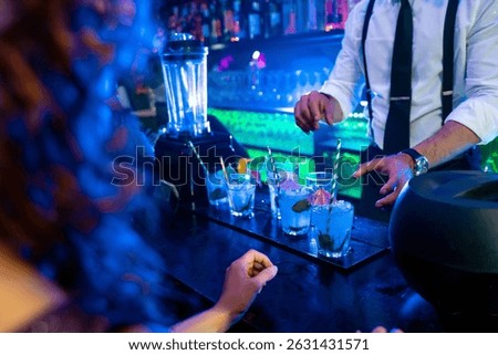 Bartender skillfully preparing vibrant blue cocktails garnished with fresh mint and ice in a lively nightclub atmosphere