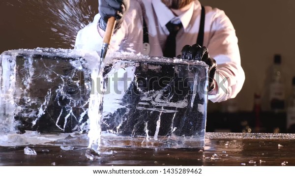 bartender splits a block of ice to cool\
cocktails, barmen splitting huge clear ice block to two parts by\
using an ice pick and\
hammer.