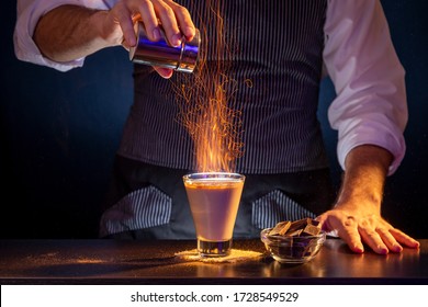 Bartender sprinkling cinnamon powder over a Baileys comet cocktail on fire, causing beautiful sparkling effect