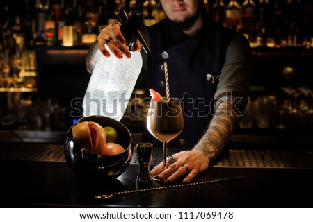 Bartender with tattoo pouring soda into the copper cocktail glass with summer cocktail, fruit and straw