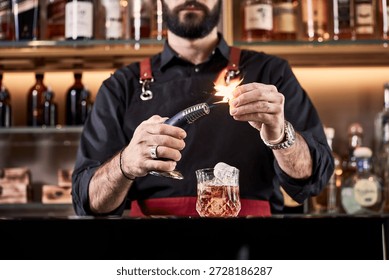 Bartender using a torch to ignite a cocktail garnish in a bar.