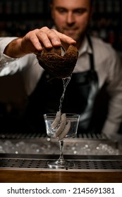 Bartender in white shirt and black apron carefully pouring a drink from a coconut into a glass decorated with coconut pieces