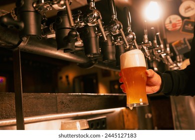 bartender's hand holds glass of light, cold, refreshing lager beer. Man Serving craft beer from tap at traditional pub. Concept of alcohol drinks, nightlife, party, festivals, Oktoberfest. Ad - Powered by Shutterstock