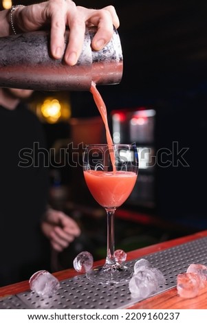 Bartender's hand pours a cocktail close-up. A glass with a long stem. The bartender prepares drinks for guests. Night life, club life. Great serving of cocktails