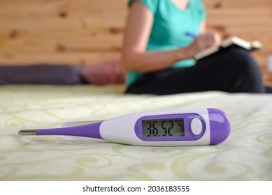 Basal thermometer with woman in background writing temperature