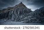 Basalt columns tower over the volcanic sand under heavy clouds in a sharp focus landscape. This shot captures the geometric beauty of Icelandic geology for nature and adventure tourism branding.