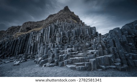 Basalt columns tower over the volcanic sand under heavy clouds in a sharp focus landscape. This shot captures the geometric beauty of Icelandic geology for nature and adventure tourism branding.
