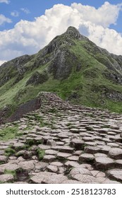 Basalt stone trail at Giant's Causeway, Northern Ireland, stretches uphill towards rocky cliffs under a partly cloudy sky, showcasing the area natural terrain