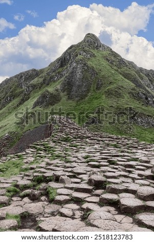 Basalt stone trail at Giant's Causeway, Northern Ireland, stretches uphill towards rocky cliffs under a partly cloudy sky, showcasing the area natural terrain