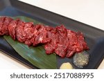 Basashi or raw horse meat sashimi with garlic and ginger sauce on black plate with white background, famous dish of Kumamoto, Japan