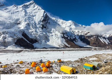 Base Camp Of High Altitude Mountain Expedition Many Orange Tents Located On Side Rock Moraine Of Glacier In Severe Snow And Ice Peaks Landscape