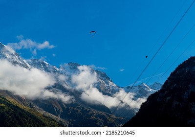 Base jumper in the distance is parachuting down to the valley in Lauterbrunnen in the Swiss Alps. Cloud covered mountains are visible in the background.