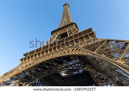Base structure of Eiffel tower in Paris, France in close look up from ground. Early golden morning light and blue sky.