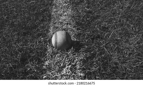 Baseball Ball On Foul Line Of Sports Field In Black And White.