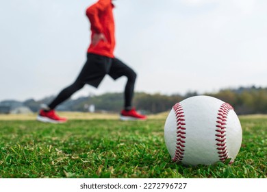 Baseball ball on grass. Man stretching in background. - Powered by Shutterstock