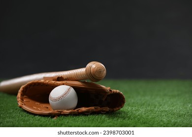 Baseball bat, leather glove and ball on green grass against dark background. Space for text - Powered by Shutterstock