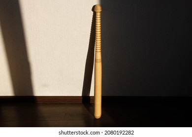 A Baseball Bat Stands Against The Wall. Beautiful Shadow Of The Sun From A Softball Bat Falls On The Wall. Sport Equipment. Carved Wooden Baseball Bat With Pattern. Copy Space For Text. Close-up