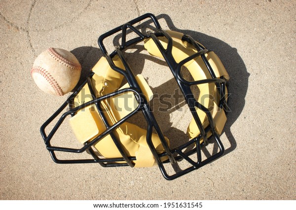 Baseball Catcher\'s\
mask and ball on\
concrete