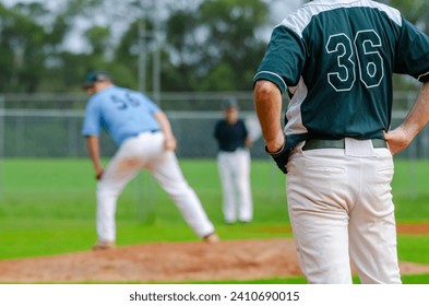 Baseball game, runner on the first base is watching the pitcher and getting ready to steal the second base.