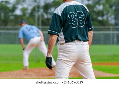 Baseball game, runner on the first base is watching the pitcher and getting ready to steal the second base.