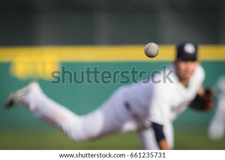 A baseball in motion with pitcher in background.