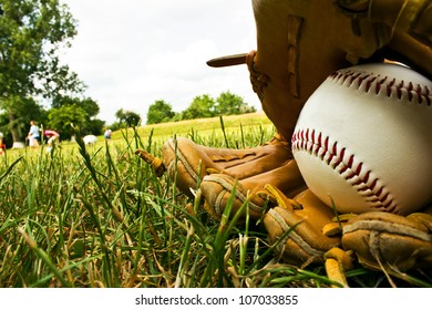  A Baseball And An Old Baseball Glove Lying On The A Baseball Field.