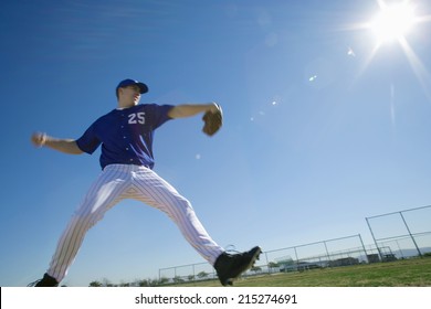 Baseball pitcher, in blue uniform, preparing to throw ball during competitive game, side view (lens flare, surface level, tilt)