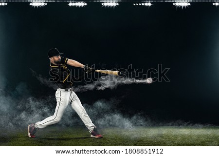 Baseball player with bat taking a swing on grand arena. Ballplayer on dark background in action.