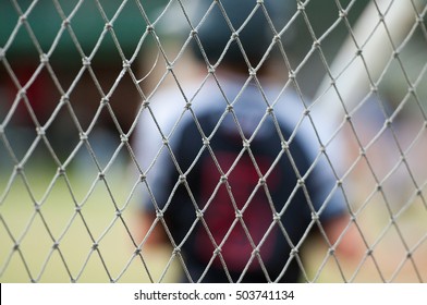 Baseball Player Out Of Focus Behind Baseball Cage Net.