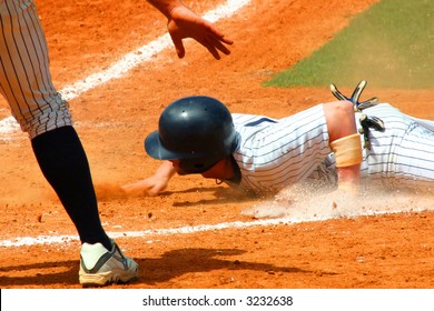 Baseball Player Slides By Home Plate With His Team Mate Signaling Safe