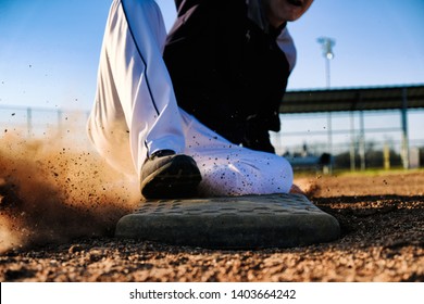 Baseball player slides into base on field closeup during sunset.  Sport action image with athlete.
