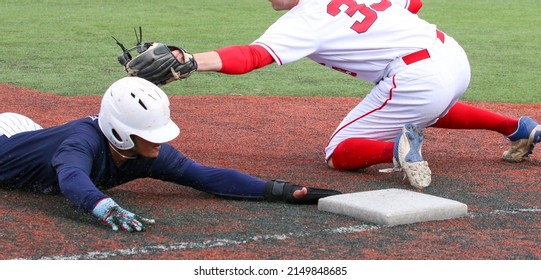 Baseball player sliding head first into third base avoiding the tag during a high school game close up.