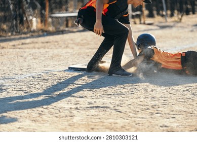 Baseball player sliding into base on a dusty field during a competitive game, showing sport action and youth activity