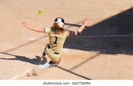 A Baseball Player Is Sliding Into Home Base While The Ball Is Flying Through The Air