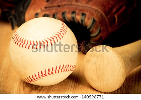 Baseball - This is a close up shot of an old baseball and wooden bad on a wood background with an old glove in the background. Shot in a warm retro color tone.