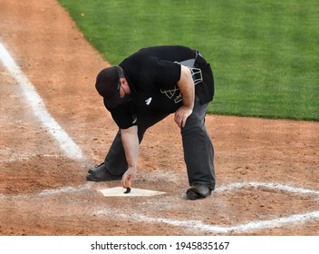 Baseball Umpire Calling Balls And Strikes At The Plate And Keeping The Home Plate Clean From Dust By Brushing It Off