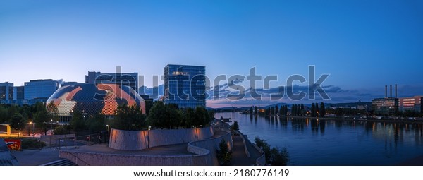 Basel, Switzerland - 16. May 2022: The new\
Novartis Pavillon at lightshow on the Rhine river bank at the\
sunset time. Novartis is a leading pharmaceutical company for\
medicine research and\
products.