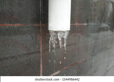 The Basement Of The Old House With A Drainpipe And Water Frozen In It. Storm Sewage On The Wall Of An Old House With Ice. Cold Snap, Winter.