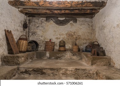 Basement Of An Old House With Wooden Beams And Wall With Humidity, Antique Household Items, Carboy Demijohn, Stewpot, Plank, Wicker Basket, Pulley With Chain, Yuguillo