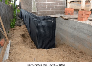 Basement waterproofing with dimple mat, dimple drain in problem corner area. House  foundation wall insulation with rigid foam board, waterproofing membrane and house foundation construction trench. 