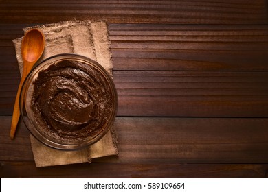 Basic Brownie, Chocolate Cake Or Cookie Dough In Glass Bowl With Wooden Spoon On The Side, Photographed Overhead On Dark Wood With Natural Light (Selective Focus, Focus On The Top Of The Dough)