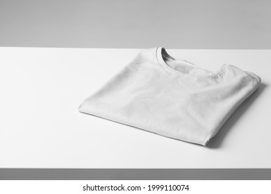 Basic Folded White Tshirt On Grey Table. Mock Up For Branding T-shirt. Monochrome Trend. 