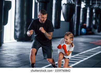 Basic punches. Young tattooed boxing coach teaches cute little girl in the gym. - Shutterstock ID 1559760842