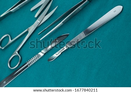 Basic surgical instrument scalpel forceps tweezers scissors spread on surgical green drape fabric
