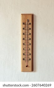 A basic thermometer on a white wall showing 20 degrees celcius.