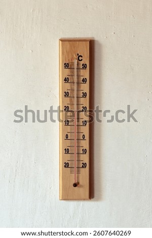 A basic thermometer on a white wall showing 20 degrees celcius.