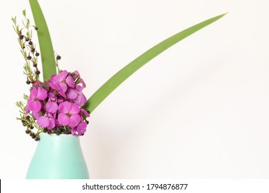 Basic white background image featuring purple wallflowers and boronia stems in small green vase with copy space