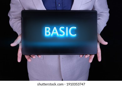 BASIC word, text written in neon letters on a laptop which is being held by a businessman in a gray suit.